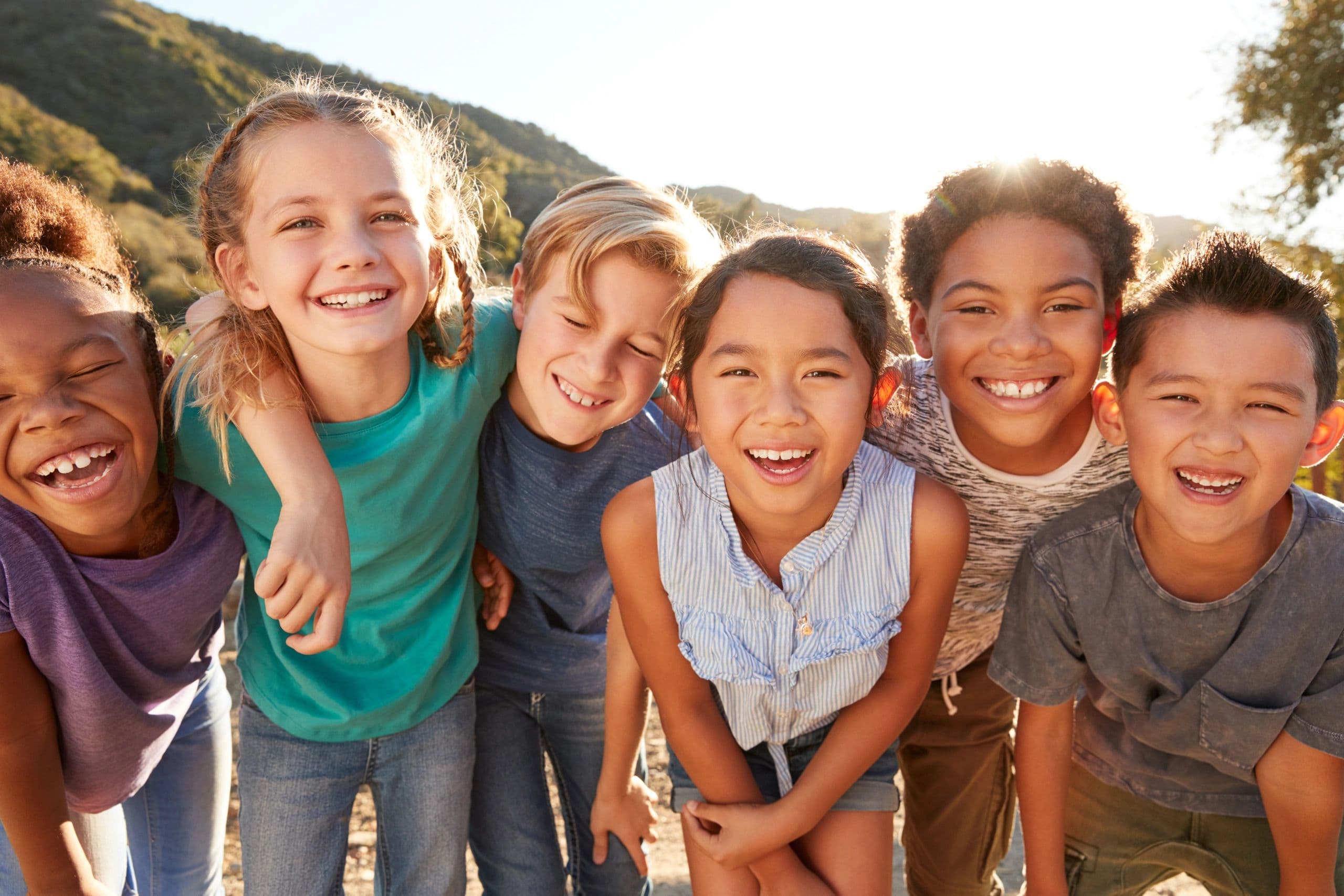 Six children laughing together outdoors on a sunny day